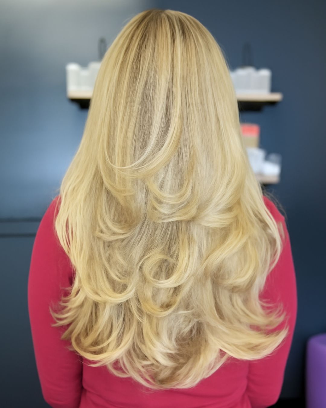 back view of a woman with long, blonde hair styled in a multi-layer haircut, showcasing soft, voluminous layers and smooth texture